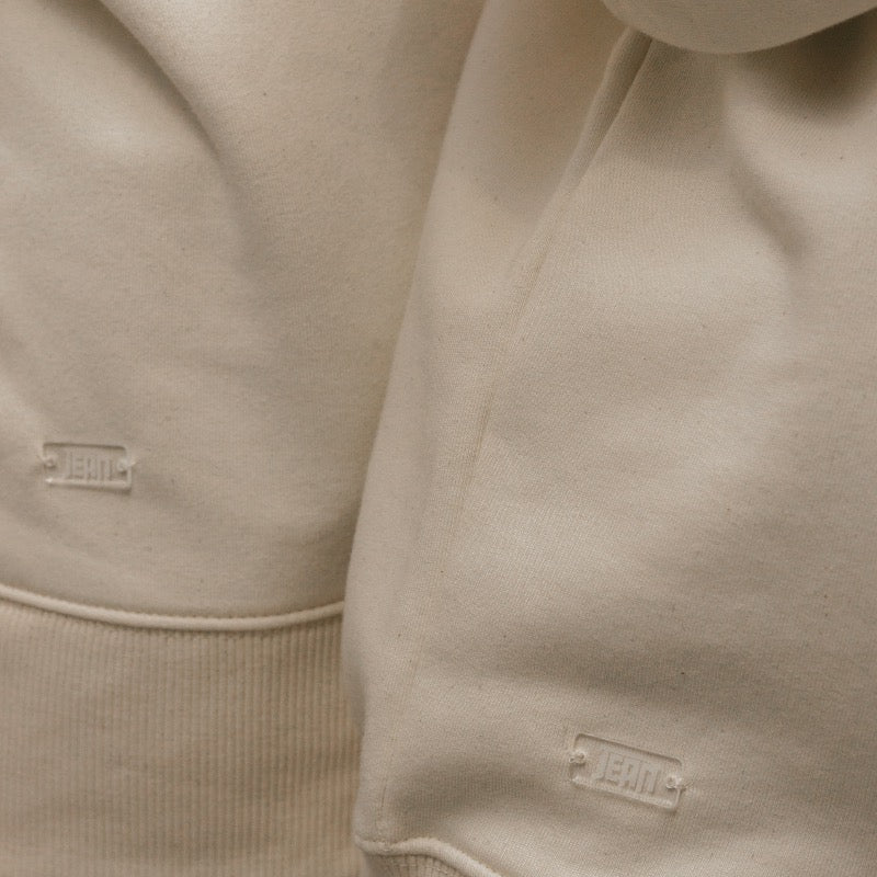 Beige sweater met beige hartje op de voorkant en oranje tekst in puff inkt op achterkant